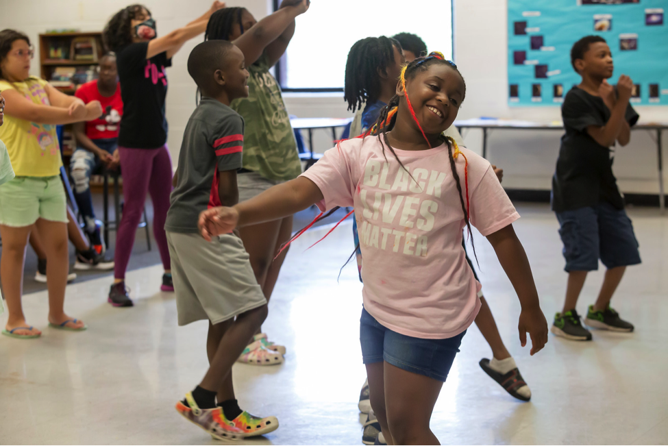 A classroom of smiling, dancing children. 
